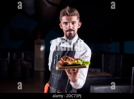 Il cordiale cameriere serve piatti cucinati nel ristorante. Foto Stock