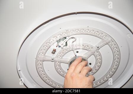 Lampada a LED sul soffitto che tiene una mano dell'uomo il centro su uno sfondo chiaro Foto Stock
