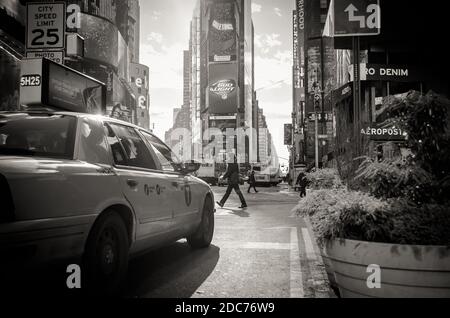 Vista su Times Square di Manhattan in bianco e nero. Un uomo sta attraversando la strada davanti a una cabina. Distretto pieno di schermi LED e pubblicità. Foto Stock