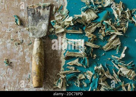 Restauro di una vecchia porta. Rimuovere i vecchi strati di vernice con una pistola termica e una spatola. Vista dall'alto . Spatola e pezzi di vernice blu arricciata. Foto Stock