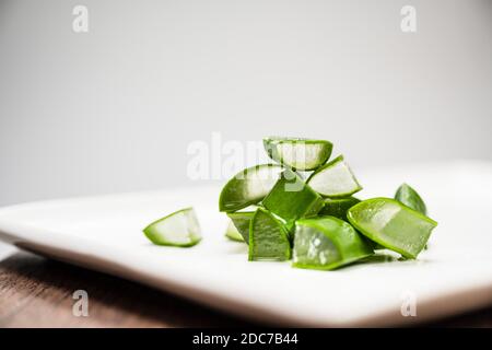 L'umidità e l'acqua sgocciolano dall'aloe fresco verde tagliato I pezzi di vera giacciono su un piatto bianco Foto Stock