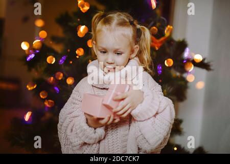 Bambina che guarda con sorpresa e gioia in giftbox aperto, albero di Natale. Foto Stock