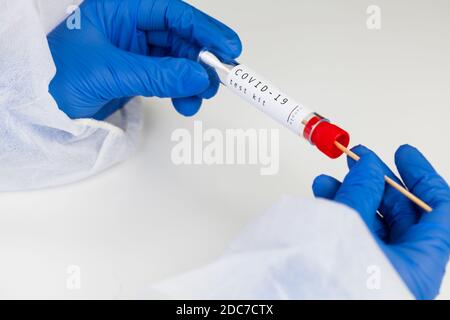 Kit per analisi Coronavirus COVID-19, apparecchiatura per il prelievo di tamponi, provetta Vacutainer sterile con bastoncino oscillante, closeup di mani in guanti di protezione blu che tengono t Foto Stock