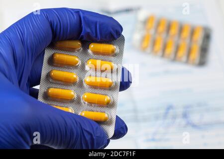 UK Doctor, infermiera, medico indossando guanti di lattice chirurgici blu che tengono giallo Pacchetto farmaci, COVID-19 malattia del virus corona epidemia, Coronavirus Foto Stock