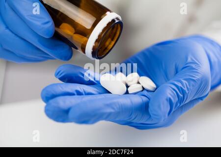 UK NHS Doctor, infermiera, medico di medicina del GP che indossa i guanti di lattice chirurgici blu Tenere flacone di medicinale, prendendo fuori diverse pillole bianche, COVID-19 corona Foto Stock