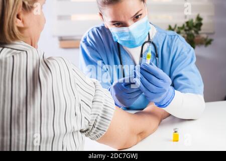 Medico GP femmina contenente fiala liquido giallo, siringa di riempimento jab Con iniezione, paziente anziano vaccinante, virus Coronavirus COVID-19 Foto Stock