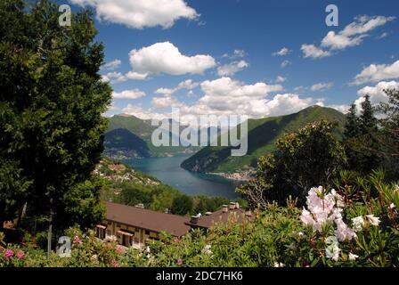 Vista sul Lago di Lugano dal Parco San Grato, Carona, Svizzera, con colline, lago e nuvole bianche Foto Stock
