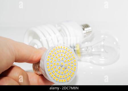 Diverse lampadine a LED e lampade fluorescenti compatte e il mano maschile su uno sfondo chiaro Foto Stock