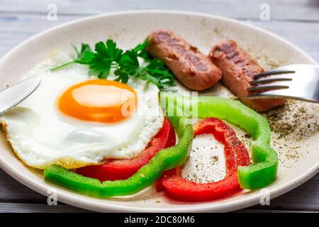 lato soleggiato in alto. Uova fritte con salsicce e verdure su un tavolo di legno chiaro. Foto Stock