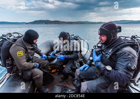 Teriberka, Russia - 29 luglio 2017: Tre subacquei seduti in barca, che controllano le loro attrezzature e si preparano ad immergersi. Sparato nel mare di Barents. Foto Stock