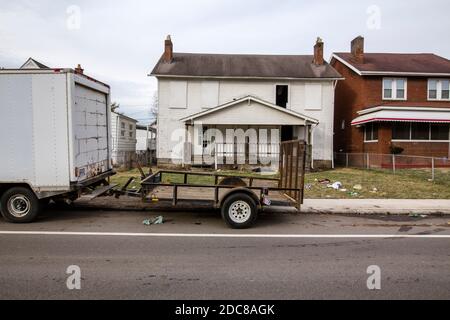 Un rimorchio a pianale si trova di fronte a casa abbandonata dentro cortile pieno di rifiuti Foto Stock