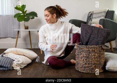 Donna si siede riorganizzando la sua pila di cuscini sul pavimento Foto Stock