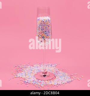 Bicchiere di champagne riempito con colorate palle di zucchero su sfondo rosa. Vetro riempito con caramelle color arcobaleno, concetto di vacanza dolce. Celebrazione, mi Foto Stock