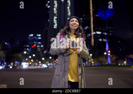 donna che visita la città scattando foto per le strade di notte Foto Stock