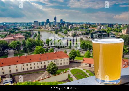 Bicchiere di birra leggera con vista dall'alto di Vilnius, Lituania. Vista areale di Vilnius, tetti rossi, fiume, grattacieli nel quartiere degli affari. Foto Stock