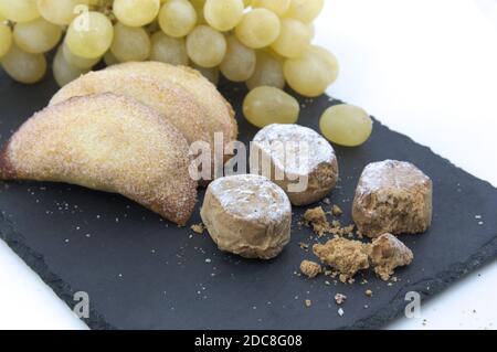 Dettaglio di un piatto d'ardesia con vari dolci tipici natalizi come torrone, uva e polvoroni su sfondo bianco Foto Stock