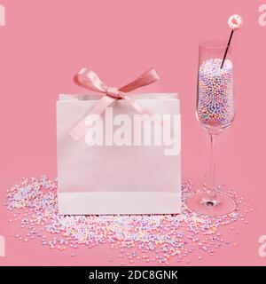 Regalo in borsa di carta bianca e vetro di campagna riempito con caramelle colorate arcobaleno su sfondo rosa. Concetto di vendita, shopping e vacanze dolci. Foto Stock