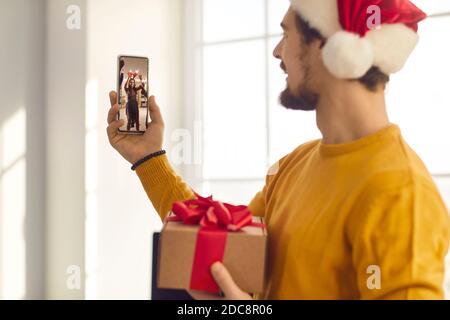Giovane uomo in Santa Hat videochiamare amici che sono Divertirsi alla festa di Natale Foto Stock