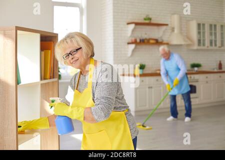 Felice uomo e donna di coppia senior in grembiuli e guanti pulizia a casa Foto Stock