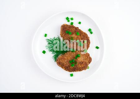 Le cotolette fritte sono cosparse di erbe in un piatto bianco su uno sfondo chiaro. Foto Stock
