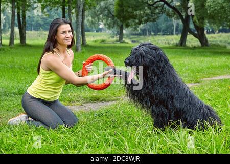 Il cane nero dà la zampa alla giovane donna nel parco mentre si siede sull'erba. Foto Stock