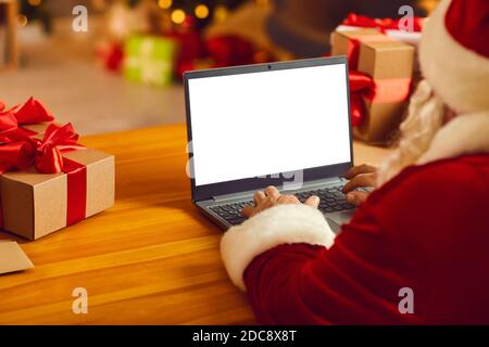 Santa Senior in costume tradizionale festivo e cappello seduta digitando Congratulazioni di Natale online su notebook Foto Stock