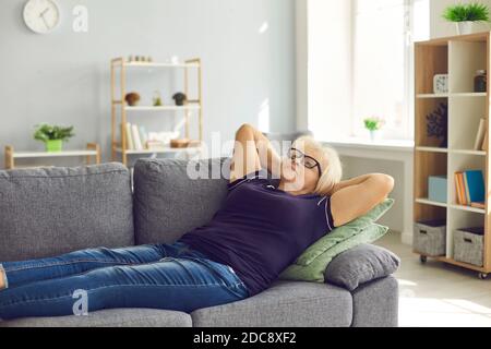 Positivo pensionato maturo donna anziana nonna mentendo e rilassandosi sopra divano Foto Stock