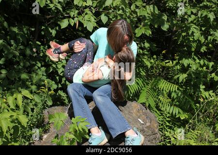 Ragazza e sua madre seduti su una roccia nel foresta che unisce ritratto Foto Stock