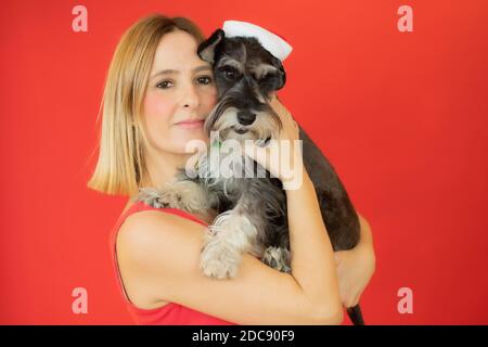 Donna sorridente e carino schnauzer con cappello santa su sfondo rosso. Foto Stock
