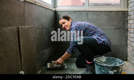 Muratore femminile che posa un nuovo pavimento di piastrelle Foto Stock