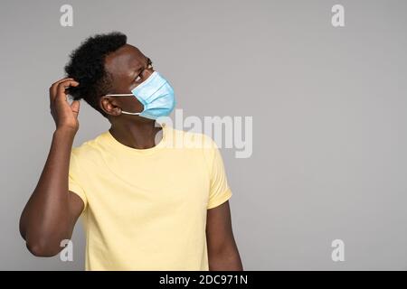 L'uomo afro-americano indossa maschera facciale, graffia la testa e pensa, guardando in su lo spazio vuoto della copia per la pubblicità, ricorda l'uso obbligatorio di un Foto Stock
