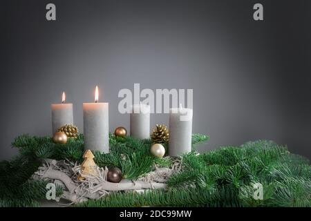 Due di quattro candele stanno bruciando per il secondo Avvento su rami di abete con decorazione di Natale contro uno sfondo grigio, spazio di copia, fuoco selezionato, Foto Stock