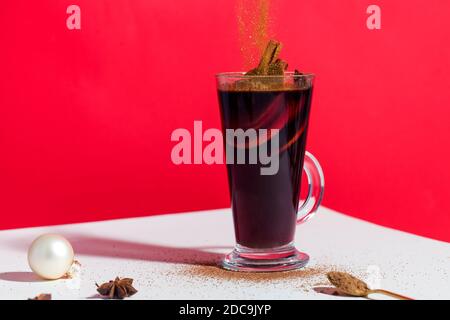 VIN brulé in un bicchiere su sfondo rosso con un giocattolo dell'albero di Natale e degli orlini che cadono. Foto Stock