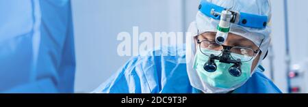 Chirurgo medico asiatico in maschera indossando loupes chirurgico durante la procedura medica, sala operatoria di chirurgia con apparecchiature di elettrocauterizzazione per cardiovascolare Foto Stock