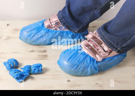 le gambe dell'adolescente con sneakers rosa e copriscarpe monouso blu su un pavimento di legno. igiene e protezione in ospedale e uffici di assistenza medica. Foto Stock