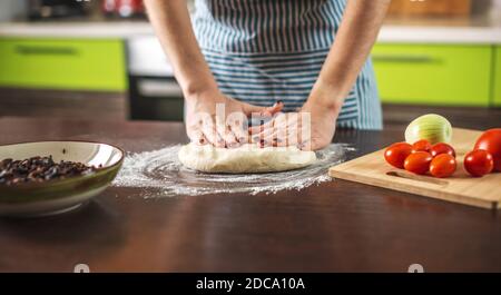Una chef femminile sta impastando l'impasto con le mani in cucina per preparare la pizza fatta in casa. Foto Stock