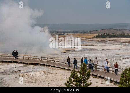 I turisti guardano il Geyser Clepsydra che emette vapore nel bacino inferiore del Geyser nel Parco Nazionale di Yellowstone, Wyoming, Stati Uniti. Foto Stock