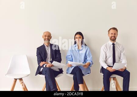 Tre candidati positivi di diverse età seduti su sedie in attesa per un colloquio di lavoro Foto Stock
