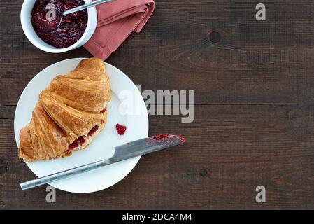 Croissant ripieno di marmellata su un piatto, con una pentola di conserve. Posto su un tavolo di legno. Foto Stock