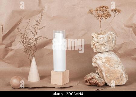 Tubo cosmetico bianco bianco con crema, siero o altro prodotto cosmetico, pietre, forma geometrica, fiori di piante essiccati su fondo di carta da artigianato beige. N Foto Stock