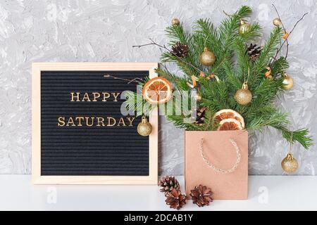 Felice testo del sabato su bordo nero della lettera e bouquet festivo di rami di abete con decorazione di natale in pacchetto artigianale e sul tavolo. Modello per postcar Foto Stock