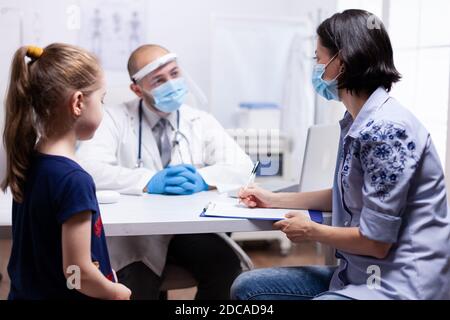 Donna che scrive prescrizione sulla clipboard ascolto medico istruzioni. Medico specialista che fornisce servizi di assistenza sanitaria consulenze trattamento in dispositivi di protezione per la consultazione Foto Stock