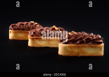 Biscotti frollini con panna di cioccolato marrone montata con mascarpone. Tre dolci freschi fatti in casa isolati su sfondo nero. Concetto di dolci, industria alimentare. Foto Stock