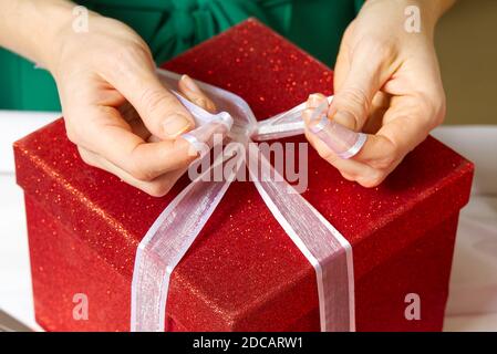 le mani della donna imballano un regalo di natale in una scatola rossa con un nastro bianco. imballaggio del regalo di diy Foto Stock