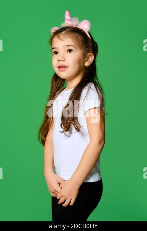 Bambino divertente con unicorno capelli cerchio sulla testa e. in t-shirt bianca e leggings neri che si posano su sfondo verde Foto Stock