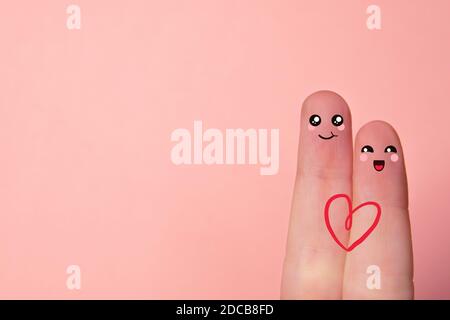 Dita d'amore. Primo piano di due dita su sfondo rosa con volti smiley disegnati. Amore e concetto di San Valentino. Copia spazio Foto Stock