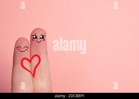 Dita d'amore. Primo piano di due dita su sfondo rosa con volti smiley disegnati. Amore e concetto di San Valentino. Copia spazio Foto Stock