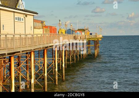 Un bellissimo molo vittoriano sul mare, ospitato con graziose capanne colorate che escono al mare nel bel sole della sera d'oro in autunno Foto Stock