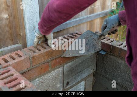 primo piano di mattoni di posa muratura con cazzuola per muratura e. malta costruzione di un barbecue fuori in estate Foto Stock