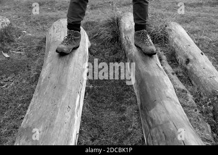 immagine in bianco e nero mans gambe e piedi su Tronchi di tronco di albero di legno all'esterno indossando scarponi da trekking.Maschile che cammina all'esterno fare esercizio in inverno Foto Stock